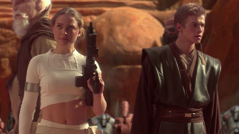 Padme holding gun and walking next to Anakin